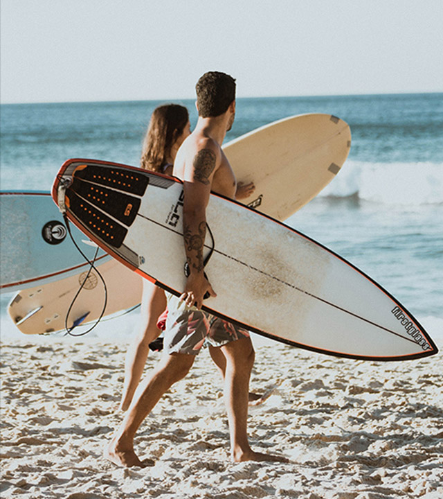 Two people walking and looking out to sea together on a sandy beach with surfboards