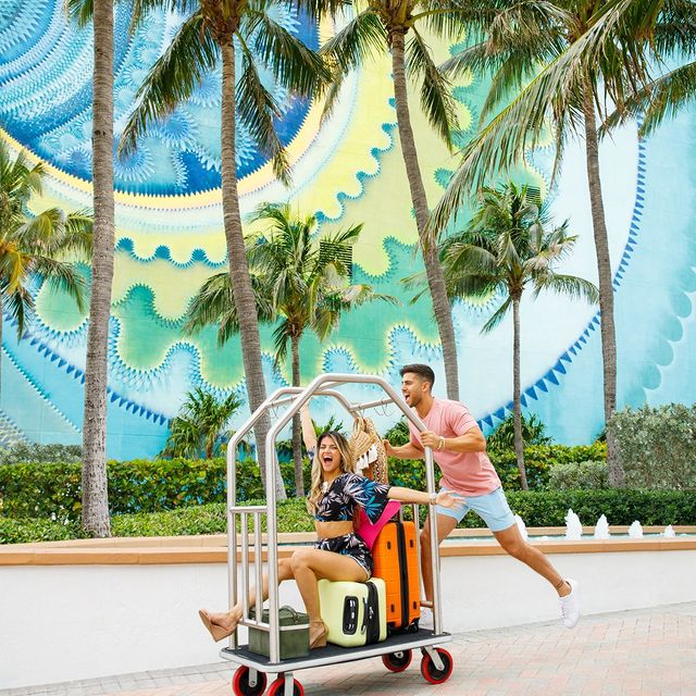 Guests riding a luggage cart in front of a mural